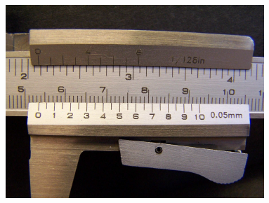 A metal ruler with centimeter and millimeter markings on the bottom and inch and eighth inch markings on the top.  Around about a two inch section of this is a larger piece of metal that can slide along the ruler.  The top of this piece has markings for 0 to 8 and is labeled 1/128 in.  These markings can line up with the markings on the inch side of the ruler.  The bottom of the larger piece of metal have markings for 1 to 10 with half markings in between.  This side is labeled 0.05 mm and the markings can line up with the centimeter side of the ruler.  Extending from the bottom of the larger piece of metal is a handle to make it easier to slide.